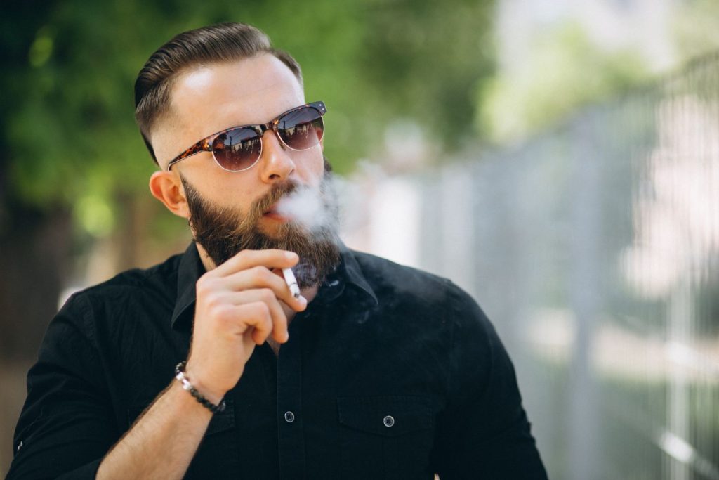 Man wearing black clothes and sunglasses smoking at a tobacco shop in Southern Plaza
