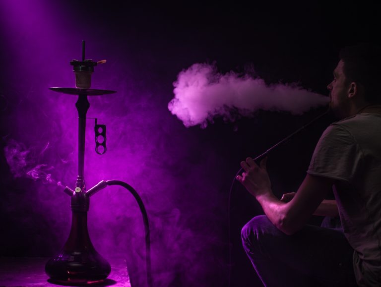 Man smoking shisha with bright light against a purple background at hookah shop in Tulsa.