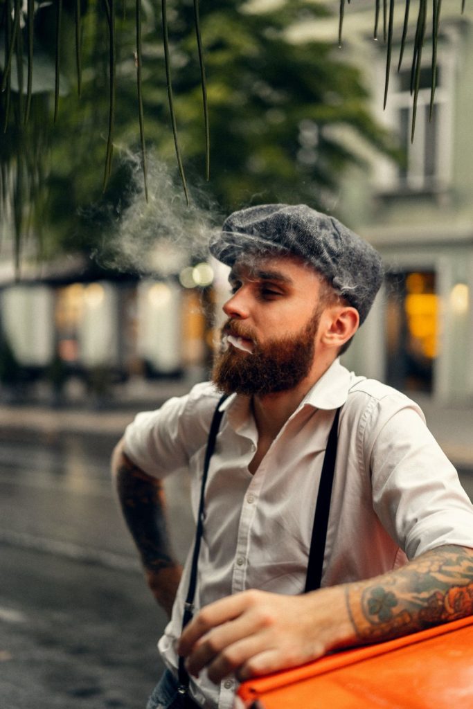 Man smoking wearing a white shirt with suspenders and a gray cap, tobacco shop in Stevenson smoking man outdoor.