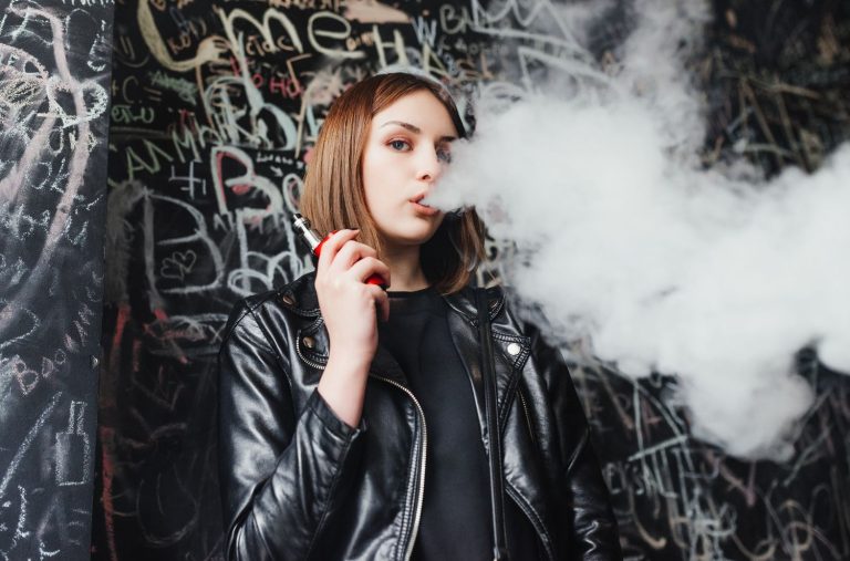 A young woman smoking vape with a Grafitti background at a Vape Store in Tulsa