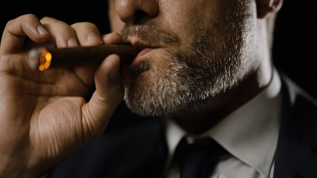 A man in a suit smokes a cigar, highlighting the luxurious vibe of a cigarette shop Tulsa.