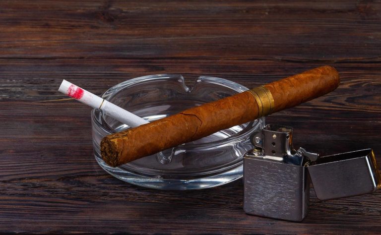 A cigar and cigarette with lipstick in an ashtray, next to a lighter, promoting a cigarette shop Tulsa.