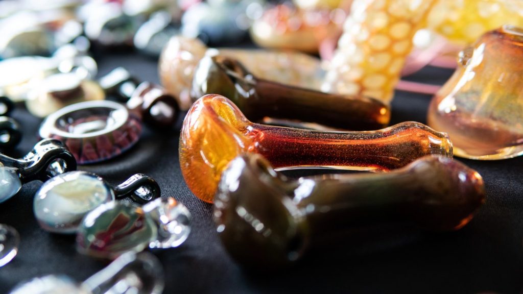 Artistic orange and amber glass pipes Tulsa alongside beaded accessories arranged on a dark surface.
