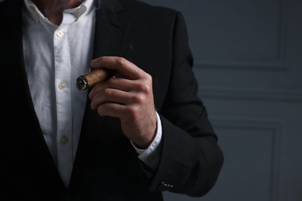 A man in a suit holds a cigar, promoting a cigarette shop Tulsa with a stylish and elegant vibe.
