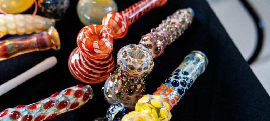 Multicolored striped and beaded glass pipes Tulsa in red, yellow, and blue laid out on black fabric.