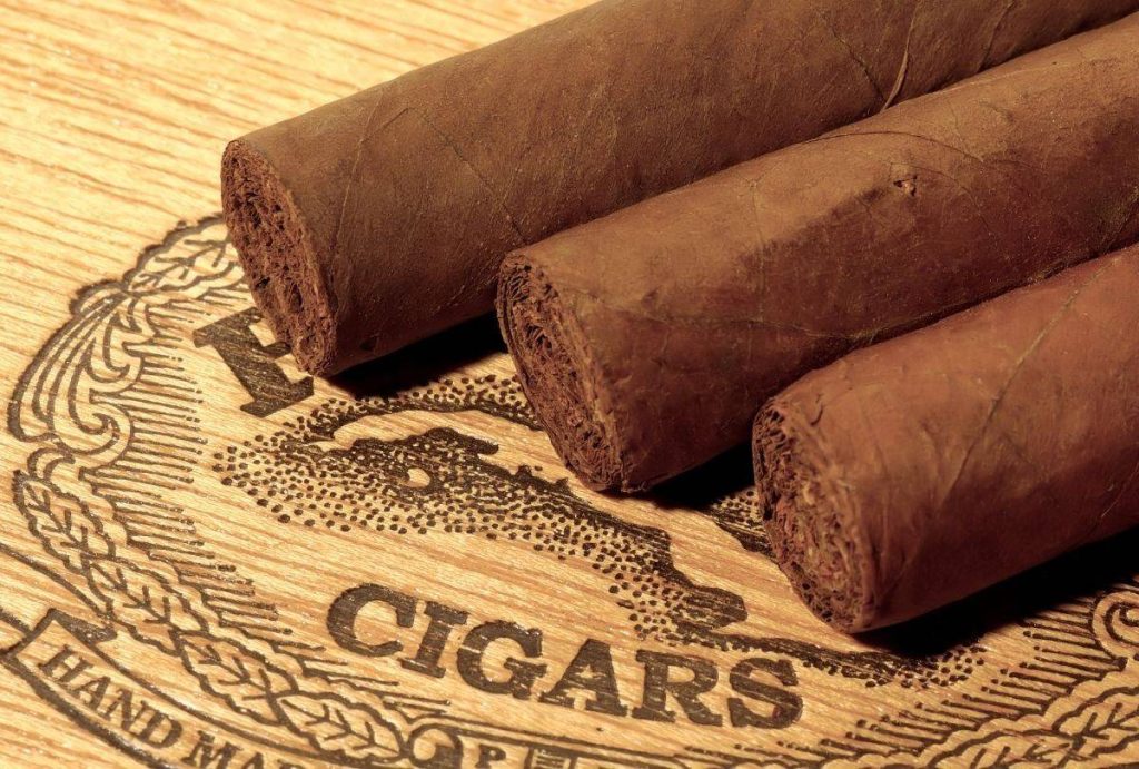 Three brown cigars on engraved wood labeled “CIGARS,” artisanal product showcase from Cigar Shop Tulsa handcrafted selection.