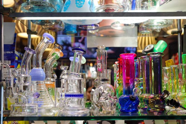 Vibrant glass bongs with percolators and themed designs on lit shelf, highlighting Head Shop Tulsa’s artisan smoking pieces.