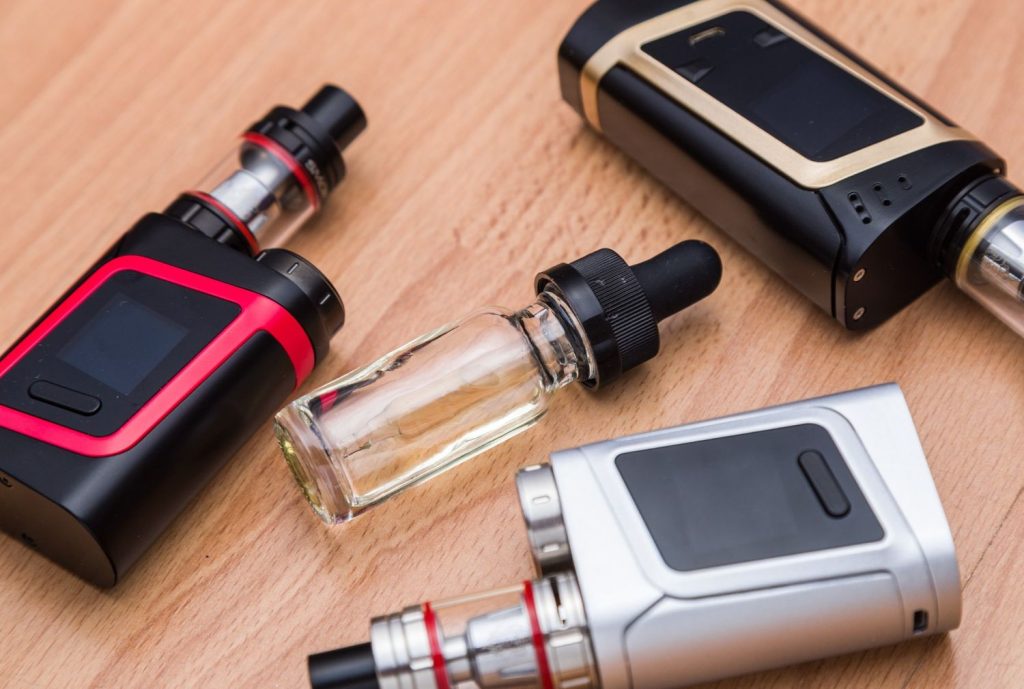 Vape mods and a bottle of e-liquid on a wooden table. High quality supplies from the best vape shop tulsa.