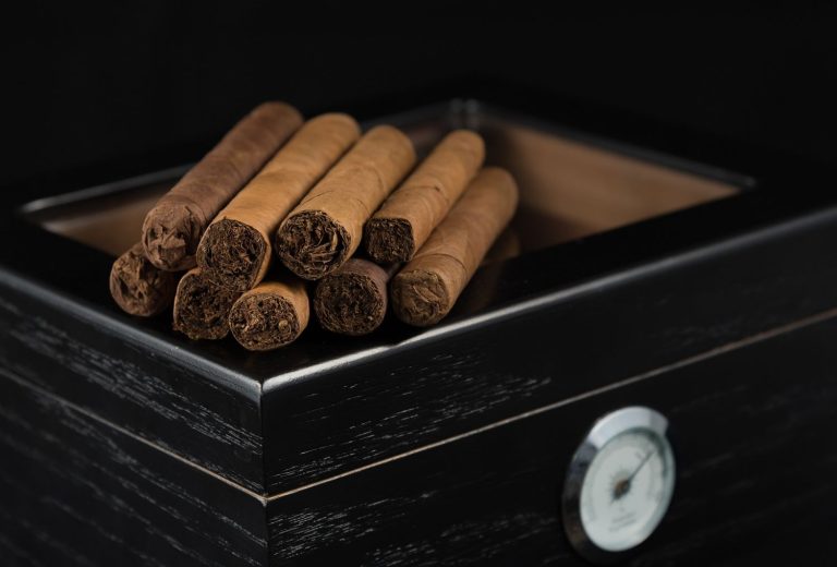 Light wrapper cigars stacked on a black humidor. Find premium accessories at this cigar shop tulsa.