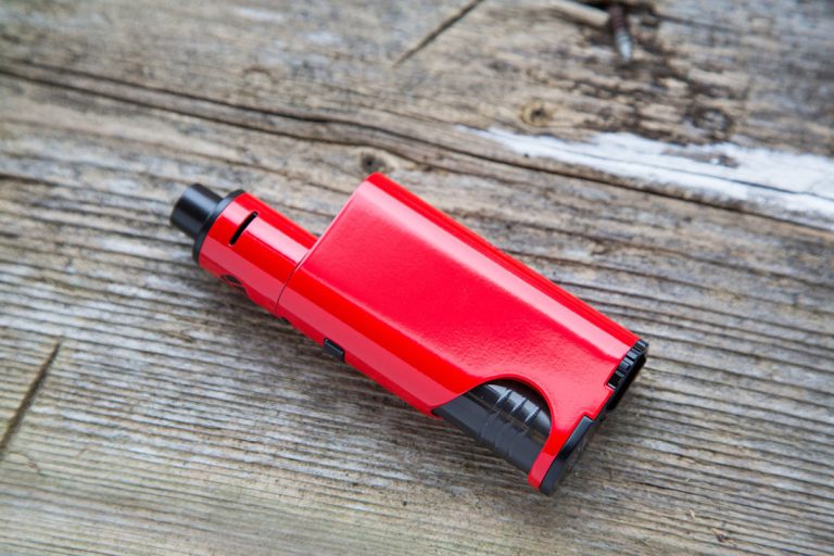Compact red box mod available at the best shop for disposable vapes Tulsa, resting on a weathered grey wooden surface.
