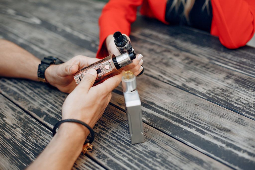 Friends sharing tips on disposable vapes Tulsa residents love while holding advanced mods at a local outdoor table. 