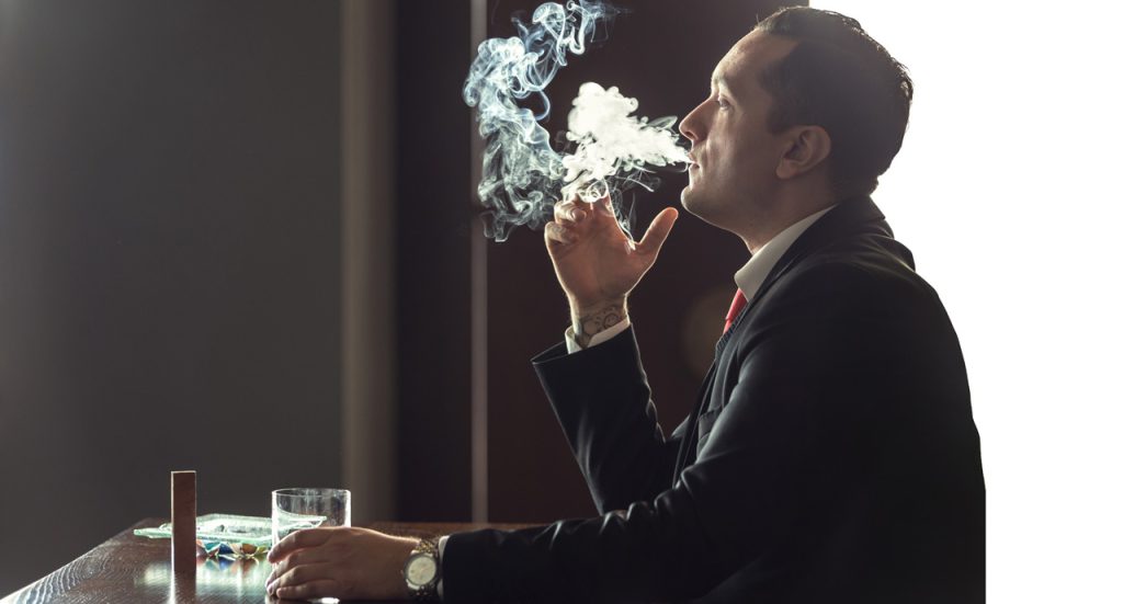 A man relaxes in a luxury cigar shop Tulsa lounge, enjoying a drink and premium smoke in a sophisticated atmosphere.