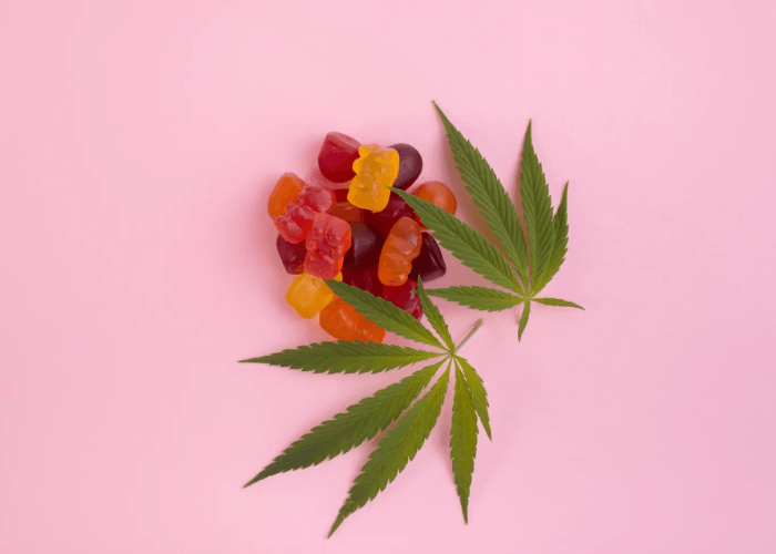 Vibrant red and orange gummy bears with cannabis leaves at a CBD shop Tulsa on a bright pink aesthetic background.