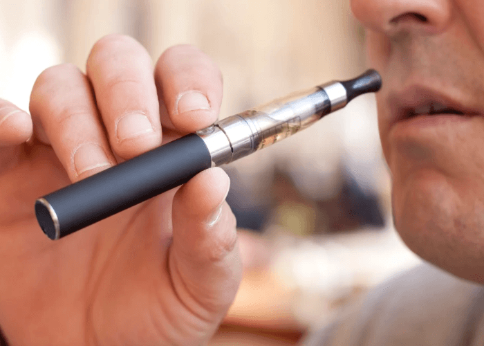 Close up of a man holding a black vape pen and e-cigarettes Tulsa device while preparing to use the handheld vaporizer.