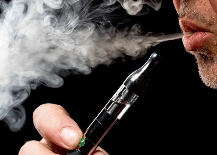 A person using e-cigarettes Tulsa products and exhaling a thick white vapor cloud from a sleek black electronic device.