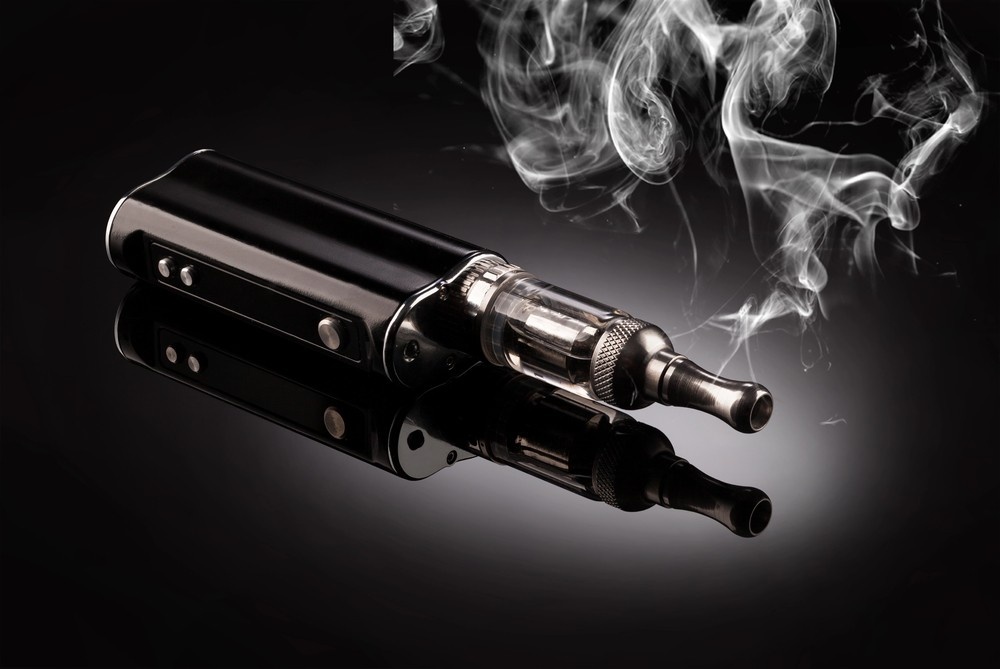 Stylish black vape mod and tank resting on a glass surface with swirling smoke. Discover quality e-cigarettes Tulsa.