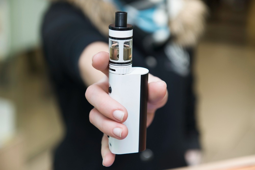 A metallic electronic mod and clear atomizer tank sit upright on wood, showing hardware from a vape store Tulsa shop.