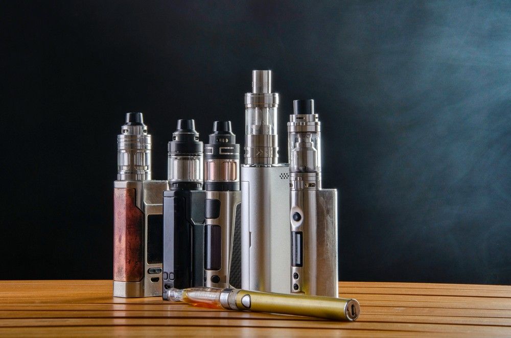 A lineup of different vape mods on a wooden table. Visit our tobacco shop tulsa for vaporizers and accessories.