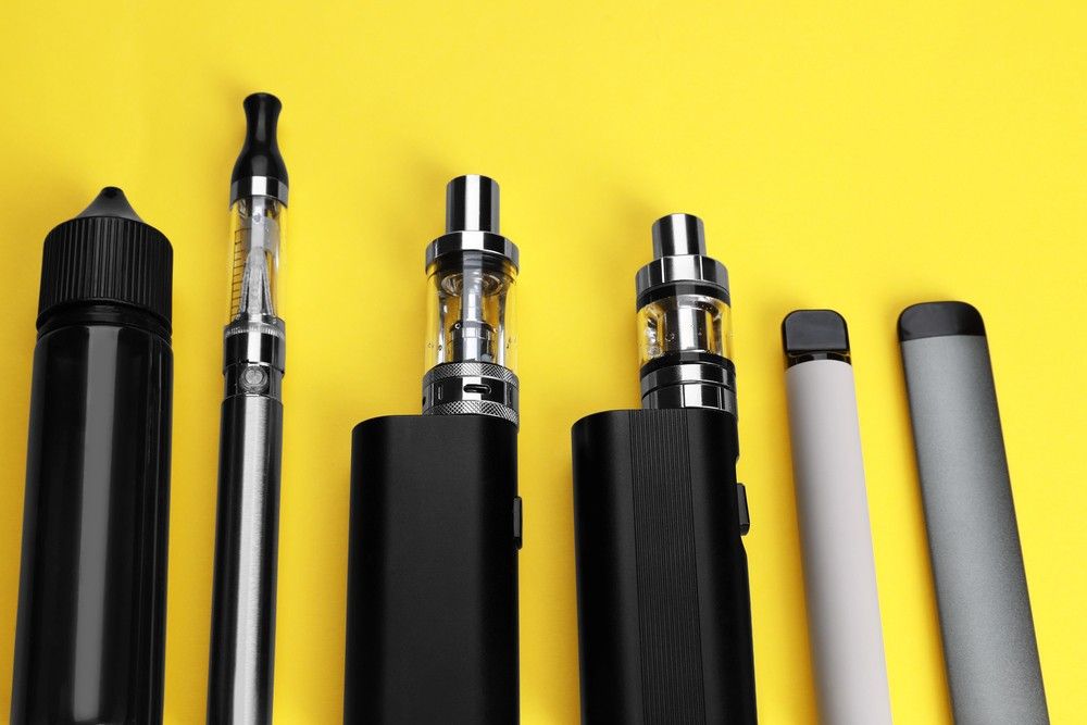 A selection of e-cigarettes tulsa devices including vape pens, box mods, and a liquid bottle on a yellow background.