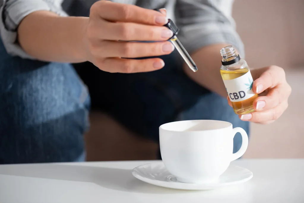 Hand adding CBD oil to tea, showcasing products from our cbd shop tulsa to help you find the perfect CBD strength.